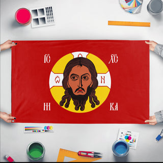 A mockup of the custom flag 'Holy Face of Christ Flag - Red flag' held up on a table during print checking
