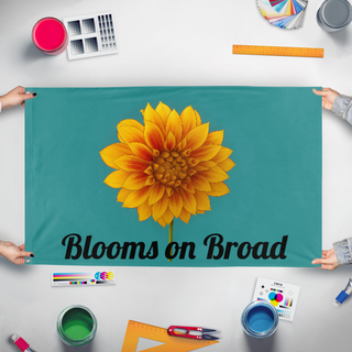 A mockup of the custom flag 'Blooms On Broad flag' held up on a table during print checking