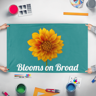A mockup of the custom flag 'Blooms on Broad flag' held up on a table during print checking